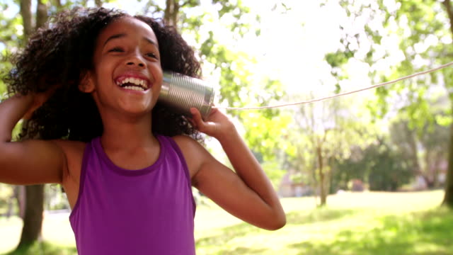 Happy Afro girl listening carefully to a tin can phone