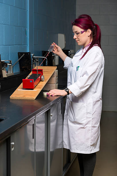 school laboratory technician a woman wearing a white coat and safety glasses is doing an experiment in a school laboratorya woman wearing a white coat and safety glasses is doing an experiment in a school laboratory dynamometer stock pictures, royalty-free photos & images