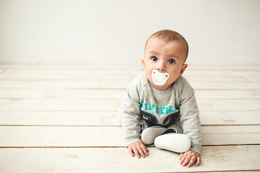 One year old cute baby boy sitting on rustic wooden floor over white background