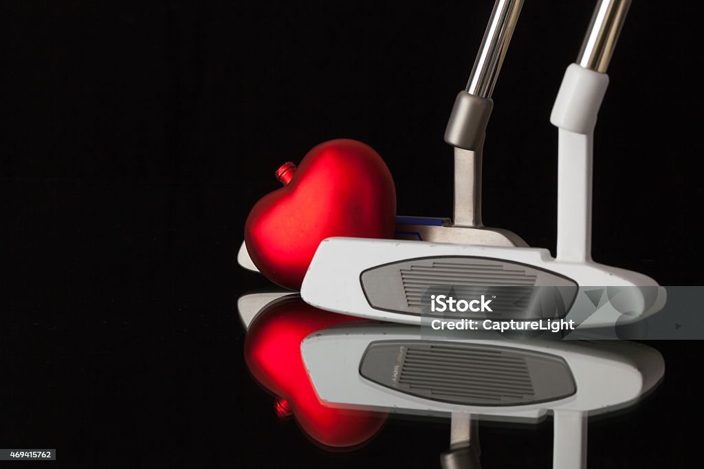 Two different golf putters and red heart Two different golf putters and red heart  on a black glass desk Emotion Stock Photo