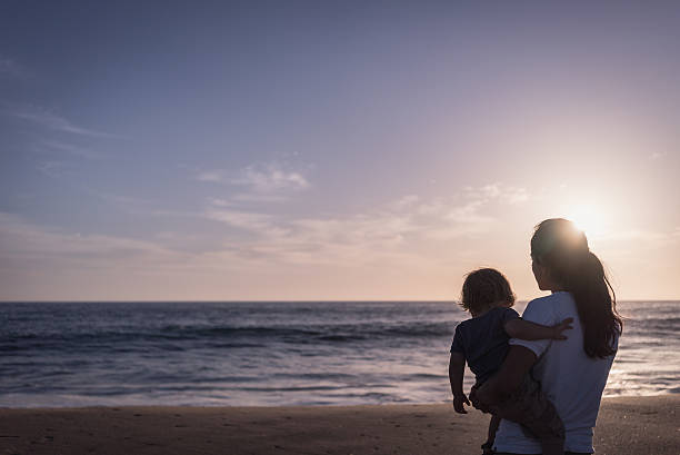 istock Women with Baby Watching Sunset on the Beach 469421468