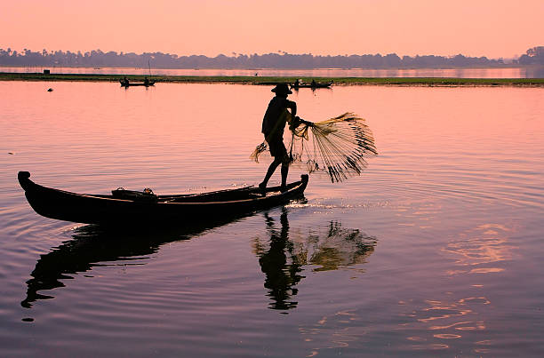 Silhouette of local man fishing with a net at sunset Silhouette of local man fishing with a net at sunset, Amarapura, Mandalay region, Myanmar u bein bridge stock pictures, royalty-free photos & images