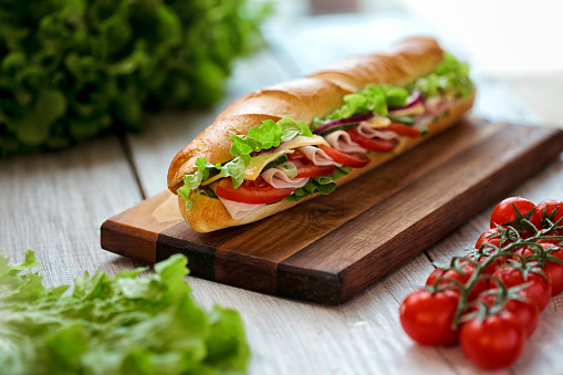  Submarine Sandwiches- Turkey, Ham and Cheese, Swiss with Lettuce , salad  and Tomato on Crusty Buns on wooden table