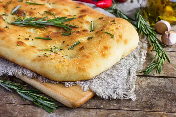 Italian focaccia bread with rosemary and garlic on a rustic background, selective focus