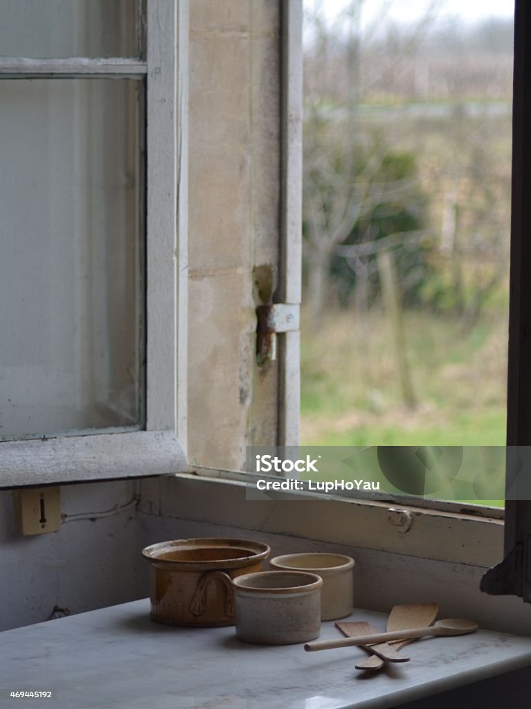 Clay pots and cooking utensils by a french farmhouse window DSLR photo of rustic clay pots, casserole dish and wooden cooking utensils by an old french farmhouse kitchen window.  The window frame is white and the marble kitchen table is grey. Outside the window, greenery of the farm is out of focus.  Farmhouse Stock Photo
