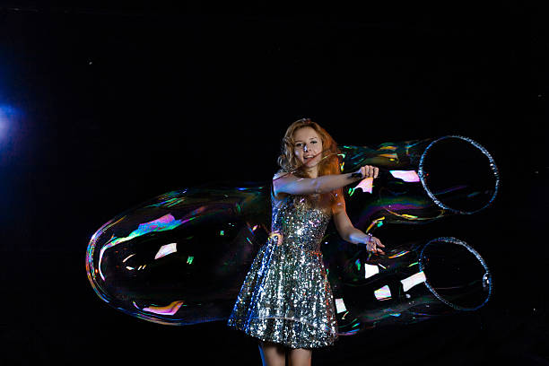 Girl performer, in a brilliant dress of sequins, inflating huge bubbles. Show bubbles, huge balls, sausages and different shapes of soap. Soap balls shimmer with rainbow colors.