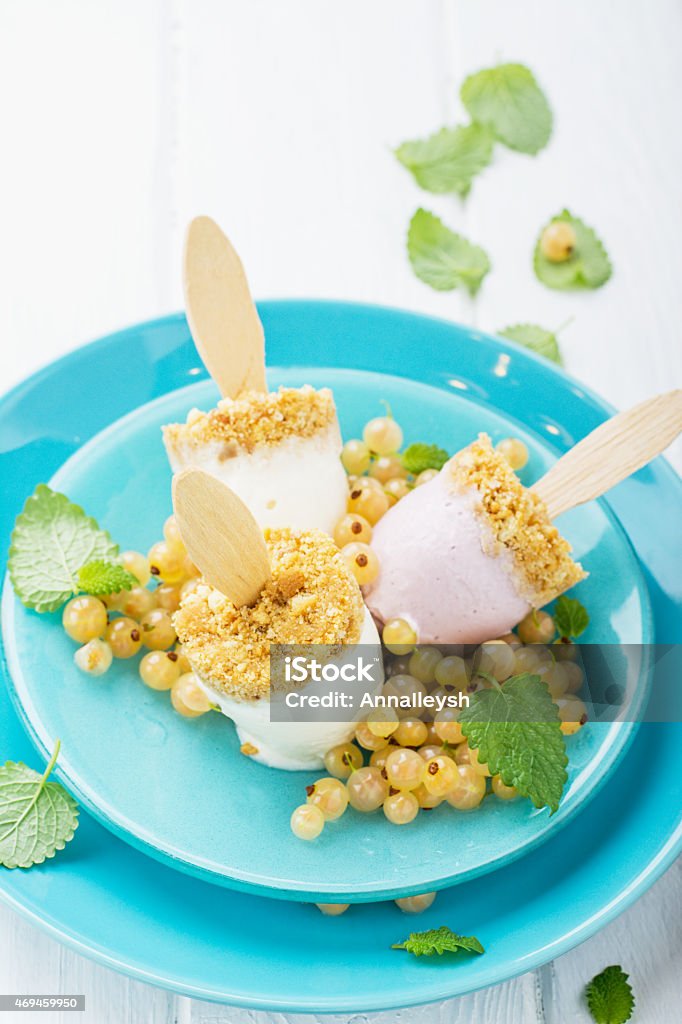 Homemade ice cream cheesecake with berries on a stick Homemade ice cream cheesecake with berries on a stick with yellow white currant berries and ice cube on a plate and a light wooden background. selective Focus Brick Stock Photo