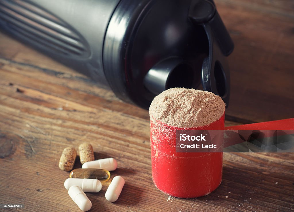 Whey protein powder Whey protein powder in scoop with vitamins and plastic shaker on wooden background Exercising Stock Photo