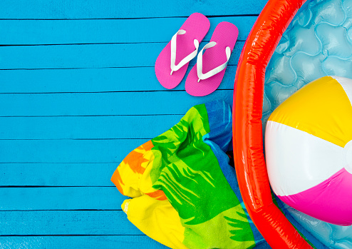 flip flops, beach ball, wading pool and beach towel on blue background