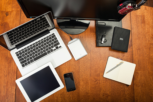 Chatham, Canada - May 22, 2014: Overhead view of a students desk. On top of the desk is an assortment of popular electronics devices. These include Apple products, iMac, laptop, iPhone, and iPad. There is an e-reader, notepad and pen. Back to school concept. There are no people in the image. 