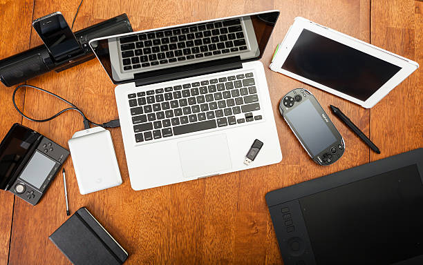 Overhead View Of Electronic Devices On A Desk Chatham, Canada - May 22, 2014: Overhead view of a students desk. On top of the desk is an assortment of popular electronics devices. These include Apple products,  laptop and iPad. There is a Playstation portable hand-held game. Also included is a Wacom drawing tablet and a hard drive. Back to school concept. There are no people in the image.  apple device stock pictures, royalty-free photos & images