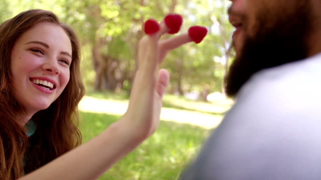 Playful girl feeding her boyfriend raspberries at a picnic