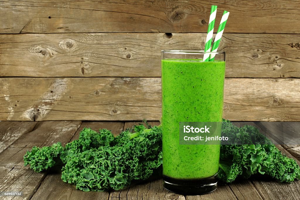 Green smoothie with kale on wood background Healthy green smoothie with kale in a glass with straws against a rustic wood background. Drinking Glass Stock Photo