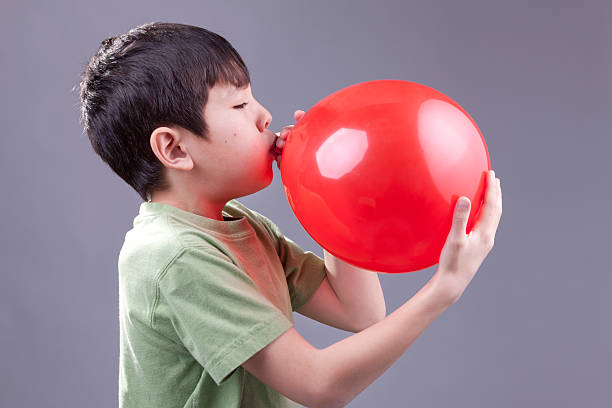 Boy blows up balloon. A young boy blows up a red baloon. inflating stock pictures, royalty-free photos & images