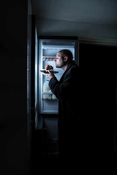 Midnight Cake Snacking a bald man in his dressing gown sniffing and savouring a slab of cake left in the fridge. midnight stock pictures, royalty-free photos & images