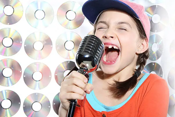 The girl singing karaoke wearing a baseball cap and orange shirt against the wall cd