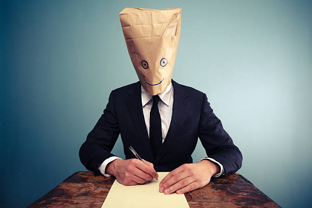 istock Businessman with bag over head writing at desk 469532389