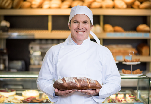 Man holding bread at the bakery and looking very proud of his new business