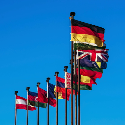 International colored flags at blue sky. Flags of European countries on the flagpole waving in the wind. In the foreground the flags of Germany and Great Britain.