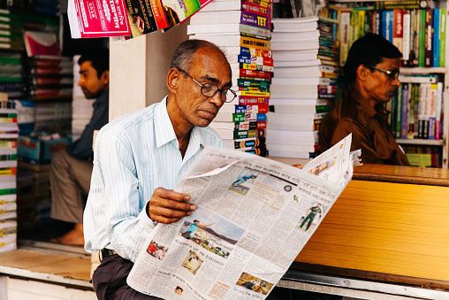 Kolkata, India - March 6, 2014: Man reading the morning newspaper while they sell used books at the largest second-hand book market in the world on College Street in Kolkata, India