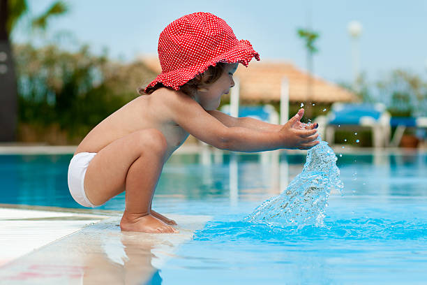 Funny little girl have a fun with a splash near swimming pool