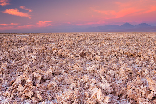 A rough salt flat with volcanoes in the distance. Photographed at the Salar de Atacama in the Atacama Desert, northern Chile, at sunset.