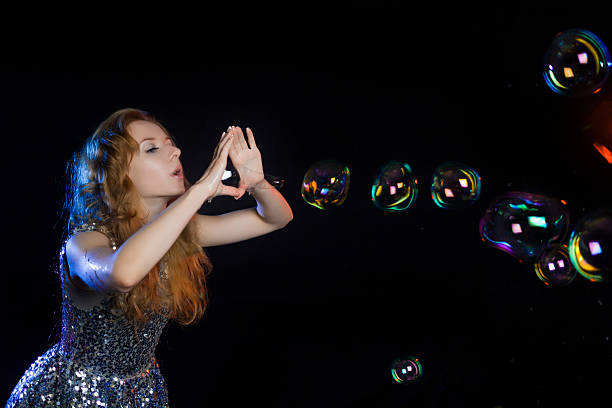 Girl performer, in a brilliant dress of sequins, inflating huge bubbles. Show bubbles, huge balls, sausages and different shapes of soap. Soap balls shimmer with rainbow colors.