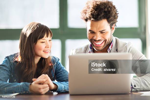 Two Young Coworkers Using A Laptop Together Stock Photo - Download Image Now - Trainee, Asian and Indian Ethnicities, Candid