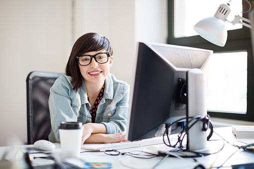 Portrait of happy young information technology professional sitting at her desk at startup company