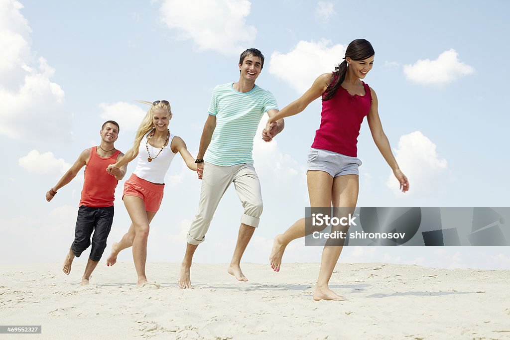 Friends on beach Four friends walking on beach holding hands Adult Stock Photo