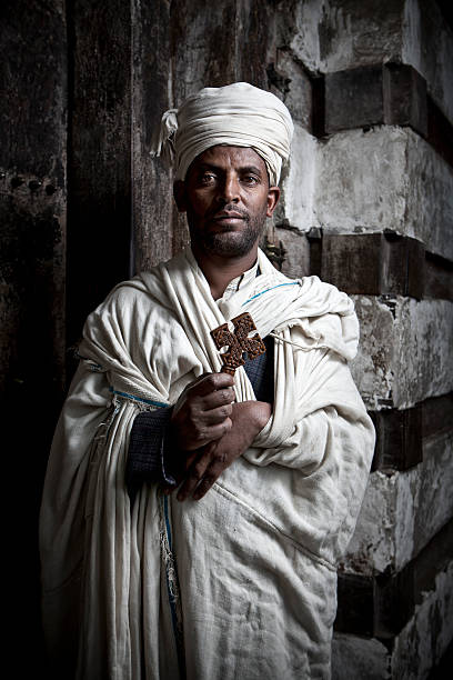 Ethiopian Priest Lalibela, Ethiopia - August 8, 2011: Ethiopian Priest in the Biete Giyorgis Church in Lalibela holds an ancient wooden cross. The church is part of the greater Lalibela church complex that is part of the UNESCO complex. A number of rock hewn churches are all linked together to make up this magical complex. the church of saint george lalibela ethiopia stock pictures, royalty-free photos & images