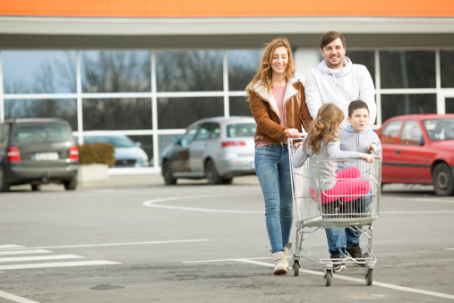 Cheerful family going to supermarket. Pushing shopping cart with children inside.