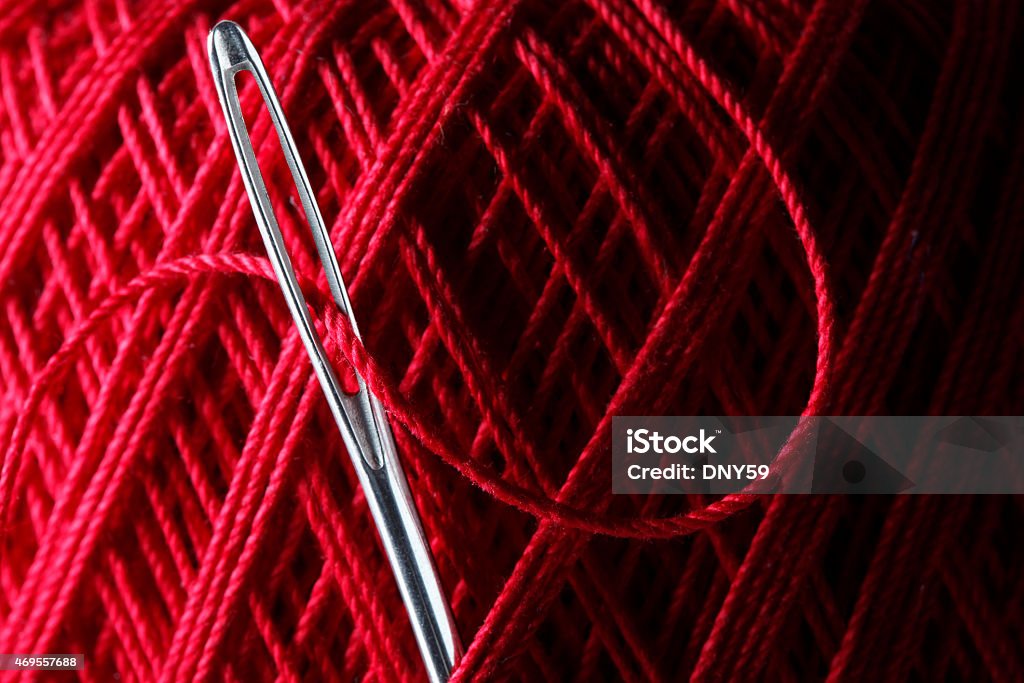 Close up of needle stuck into red ball of thread A close up of a needle stuck into a large ball of red thread.  The eye of the needle is gracefully thread and has been placed into the ball of thread for safe keeping until it is once again needed. 2015 Stock Photo