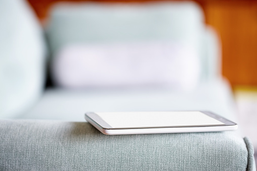 Close-up of smart phone on armrest of sofa at home. Sofa is of gray color. The focus is on the phone.