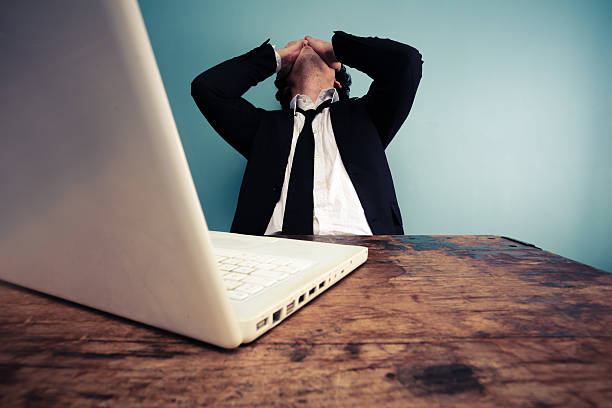 Upset businessman using a laptop Upset businessman sitting at desk with his laptop signs and symbols stock pictures, royalty-free photos & images