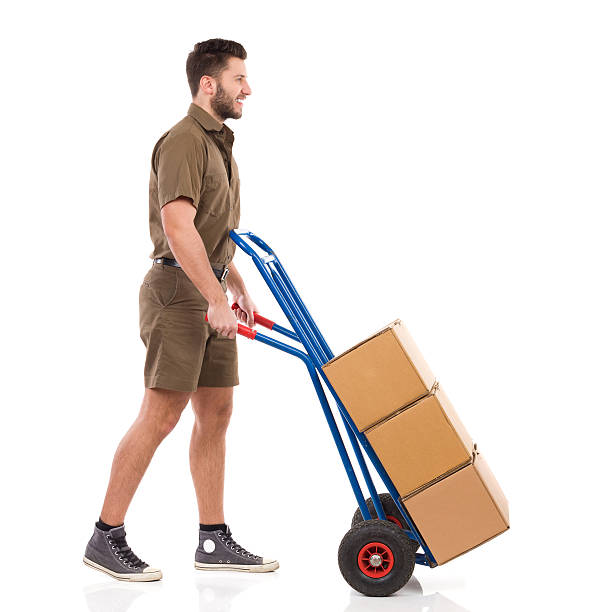 Delivering the packages Happy courier walking with a push cart. Full length studio shot isolated on white. mover delivery person box hand truck stock pictures, royalty-free photos & images