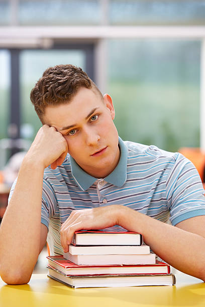 istock Unhappy Male Student Studying In Classroom With Books 469560359