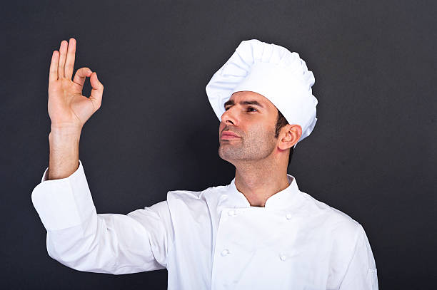 Male chef kissing fingers against grey background stock photo