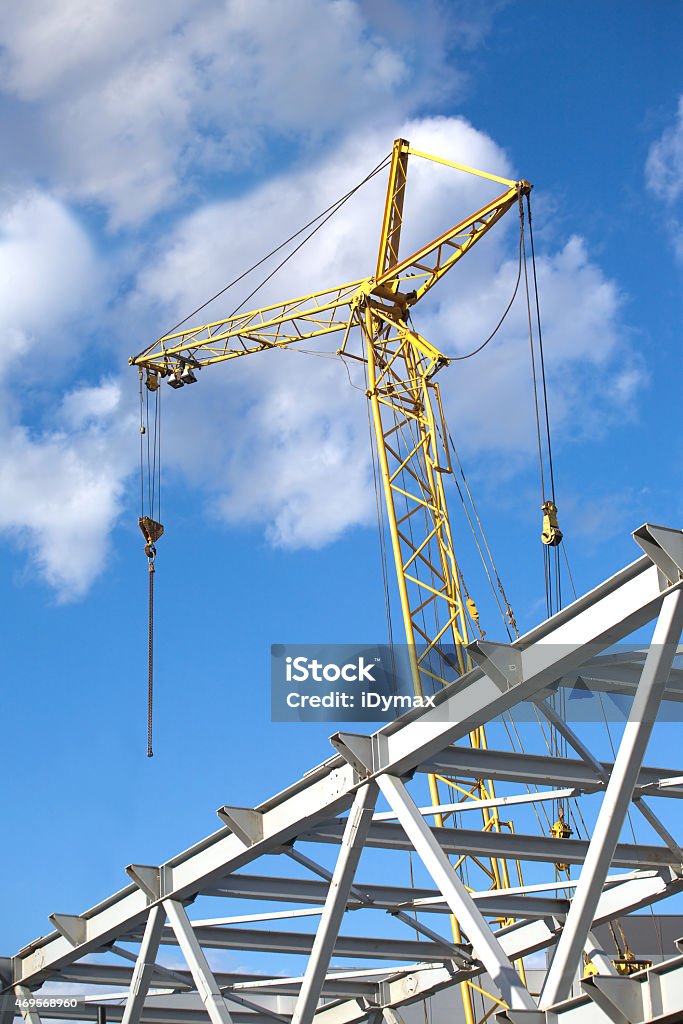 Tower crane on industrial building construction Tower crane on industrial building construction over blue sky with clouds vertical view 2015 Stock Photo