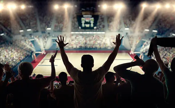 Basketball fans celebrating at a basketball game. We see their silhouettes and fans attributes