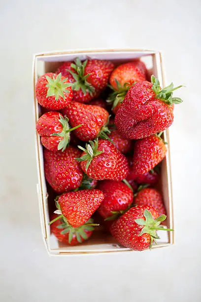 A carton of fresh strawberries on a marble table, viewed from directly above.