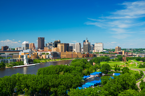 Saint Paul, Minnesota skyline with the Mississippi River, a riverfront park full of trees, a small harbor, a bridge, and a blue sky with clouds.  Saint Paul is part of the Minneapolis / Saint Paul Twin Cities Metropolitan area.