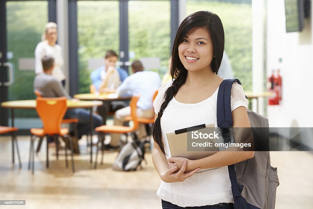 Female student with backpack in a cafeteria background Portrait Of Female Student In Classroom With Digital Tablet Smiling At Camera Filipino Ethnicity Stock Photo