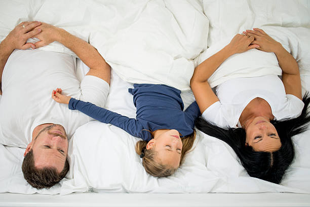 famille relaxant au lit - sleeping lying on back couple bed photos et images de collection