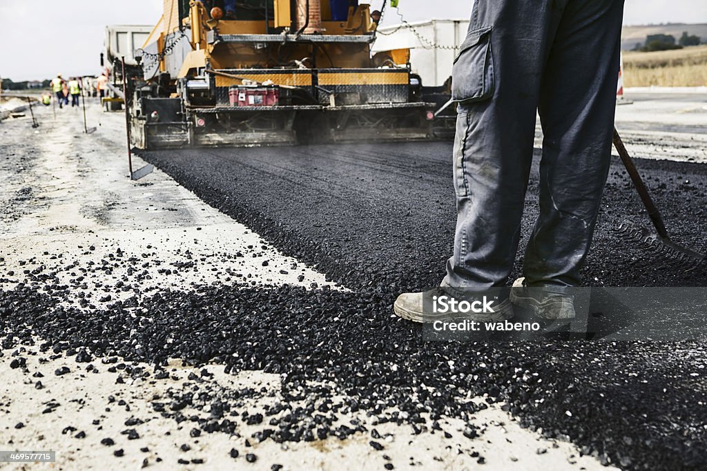 Man's legs on newly laid asphalt during road construction Worker operating asphalt paver machine during road construction and repairing works Asphalt Stock Photo