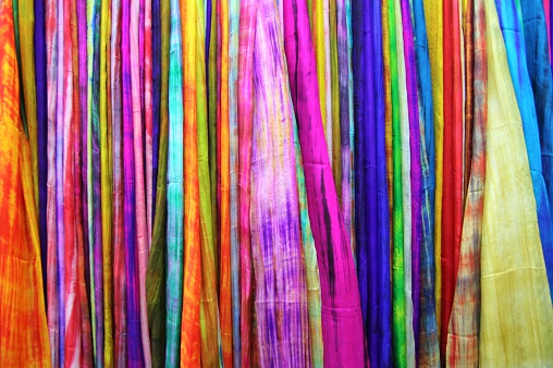 Stock photo showing close-up view of outdoor market display of hanging colourful rainbow sarong fabric.