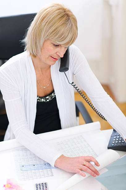 istock senior architect woman speaking phone and looking on blueprints 469587926