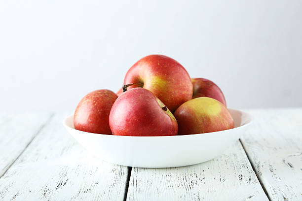 istock Apples in bowl on white wooden background 469591100