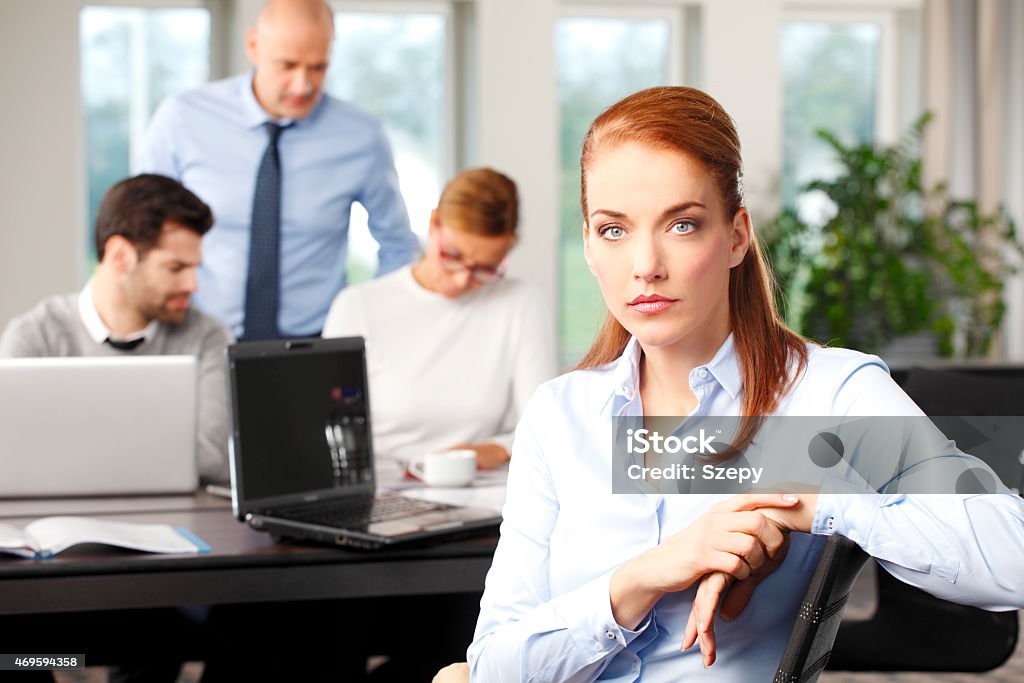 Middle age business woman Portrait of attractive business woman sitting at meeting and  looking at camera, while her staff working at background. Teamwork at office.  Businesswomen and businessmen planning the future. 2015 Stock Photo