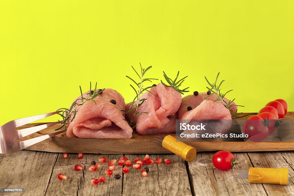 Raw Turkey Meat Wooden board with pieces of raw turkey meat, decorated with cherry tomatoes, rosemary, juniper berries and pomegranate. Backgrounds Stock Photo